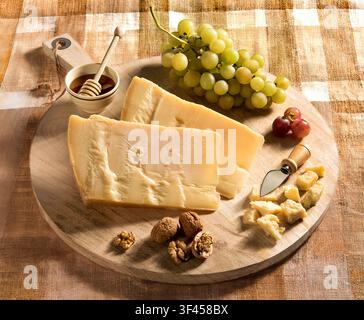 Parmesan cheese, grapes, walnuts, and honey arranged on a round wooden cutting board Stock Photo