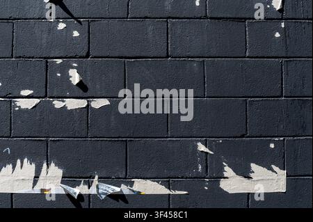 Dark brick wall finding texture from torn paper remnants and hard shadows under sunlight Stock Photo