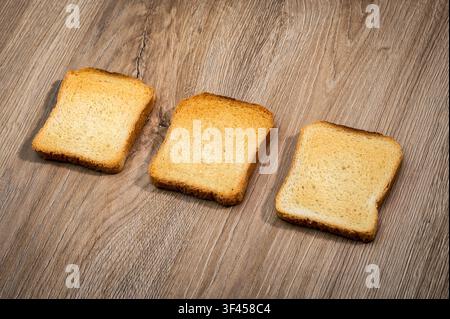 Three crispy rusks aligned on a light brown wooden tabletop, presenting a simple breakfast or snack Stock Photo