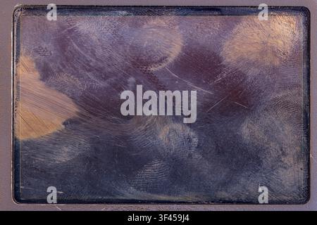Abstract macro shot reveals a dusty, smudged device screen surface with visible fingerprint patterns. The dark material showcases intricate textures a Stock Photo