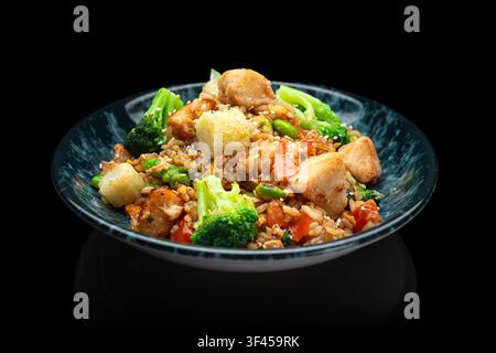 Gourmet Asian fried rice with crispy tofu, broccoli, edamame, tomato and sesame in blue ceramic bowl, black background. Vegan fusion cuisine. Stock Photo
