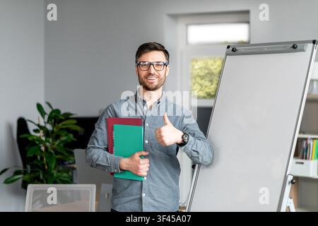 Smiling Young Caucasian Businessman Holding Folders, Giving Thumbs Up In Modern Office, Business Concept Stock Photo