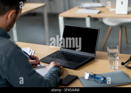 Unrecognizable Man Taking Notes On Laptop In Office Setting, Focused On Work Concept Stock Photo