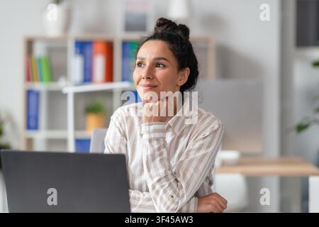 Thoughtful Young Hispanic Woman Working On Laptop In Modern Office, Business Concept Stock Photo