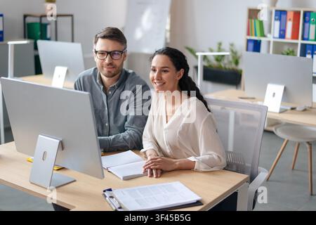 Happy Young Woman And Man Working Together At Computer In Modern Office, Business Concept Stock Photo