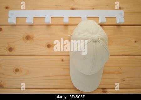 Beige baseball cap hanging on white wall hook attached to wooden plank background. Minimalist interior design detail. Accessory storage organization i Stock Photo