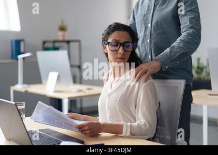Worried Hispanic Woman In Office Receiving Support From Male Colleague, Business Concept Stock Photo