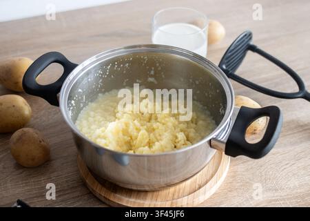 Mashed potatoes in saucepan with fresh potatoes and milk on kitchen counter Stock Photo
