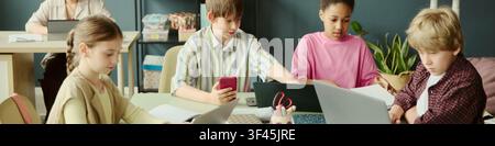 Header of children using laptops and smartphone while collaborating in classroom, learning digital skills and teamwork. Useful for education technology, coding classes, online learning campaigns Stock Photo