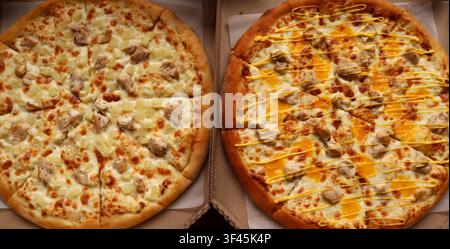 Two round pizzas in cardboard boxes. On the left is a classic Hawaiian pizza with chicken and pineapple pieces on mozzarella cheese. Stock Photo