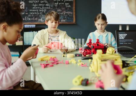 Multiethnic children assembling robotics models and testing controller during coding class, developing STEM teamwork skills. Ideal for education technology, makerspace, innovation marketing Stock Photo