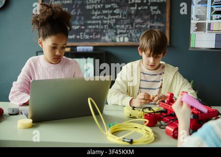 Multiethnic kids learning coding and robotics, using laptop and assembling device in classroom. Supporting STEM education, digital skills training, school marketing campaigns Stock Photo