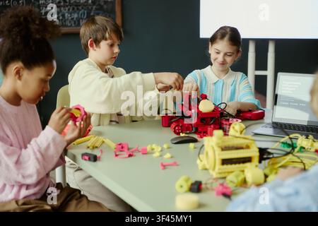 Diverse children assembling robotics models during classroom coding lesson, learning engineering teamwork and STEM skills. Ideal for education marketing, edtech promotion, STEM programs Stock Photo