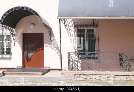 Forged iron railing window bars entrance. Vintage metal porch awning and decorative security grill cast sharp shadows on pink building facade wall. Ol Stock Photo