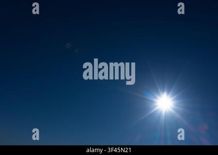 A bright sunburst radiates in a deep clear blue sky, producing vivid lens flare and warm summer sunlight. The minimal composition evokes warmth, optim Stock Photo