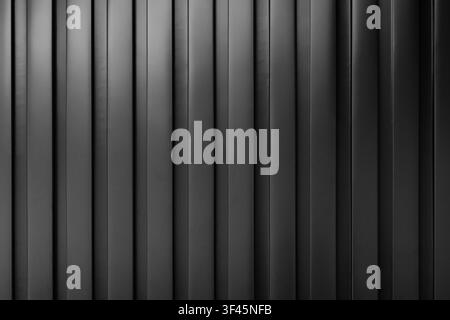 Black metal vertical panels create a minimalist, industrial wall texture with repeating lines and subtle shadows. Clean geometric pattern ideal for ba Stock Photo