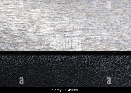 Closeup of a brushed metal plate above a rough textured black surface, highlighting industrial contrast, minimal composition and detailed material tex Stock Photo