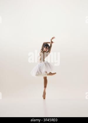 Elegant young brunette ballerina balancing en pointe in white tutu with raised arms Stock Photo