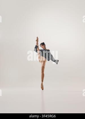 Flexible young brunette ballerina performing extreme high leg extension in black costume Stock Photo