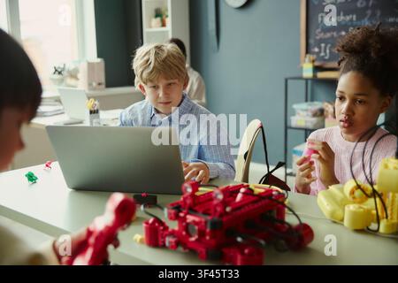 Diverse kids learning coding and robotics with laptop in classroom, building STEM teamwork and problem solving skills. Useful for education technology, STEM programs, digital learning Stock Photo