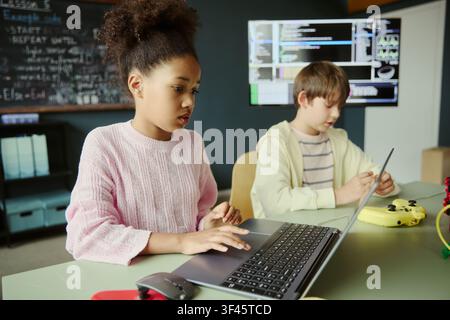 Black girl kid using laptop while Caucasian boy kid programming device in coding class, showing STEM learning and digital skills. Useful for education technology and youth training campaigns Stock Photo