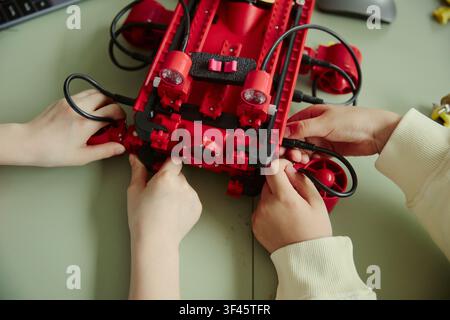 Close up of kids assembling underwater robot, connecting cables during STEM classroom project, learning engineering teamwork. Ideal for education technology, coding, robotics promotion Stock Photo