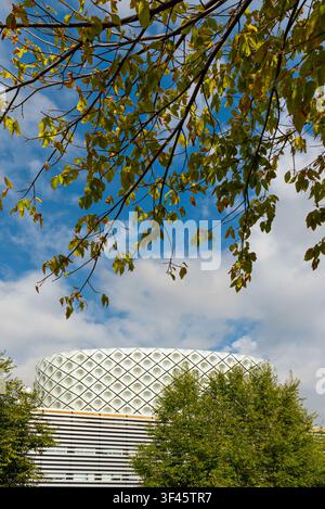"Circular Perforated Building Framed by Overhanging Autumn Leaves Against Bright Blue Sky" Stock Photo