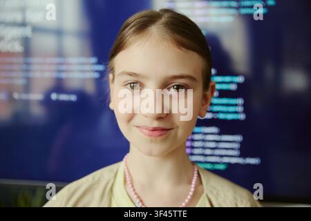 Portrait of Caucasian girl looking at camera with coding interface behind, representing early STEM learning and digital skills. Useful for education, technology, youth coding campaigns Stock Photo