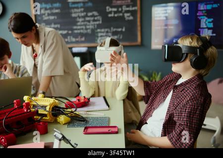 School children using virtual reality headsets during STEM lesson with teacher, exploring immersive technology and coding concepts. Ideal for education innovation and edtech marketing Stock Photo