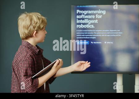 Caucasian schoolboy presenting robotics programming on digital screen while holding tablet in classroom, showing STEM learning and coding skills. For education technology campaigns Stock Photo