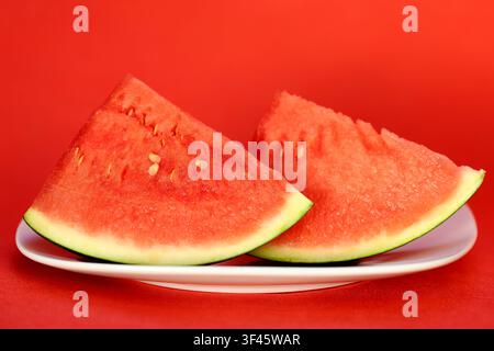 Two fresh juicy slices of red watermelon on a white plate against red background Stock Photo