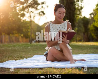 Asian woman enjoys reading a book in a park on summer day. Stock Photo