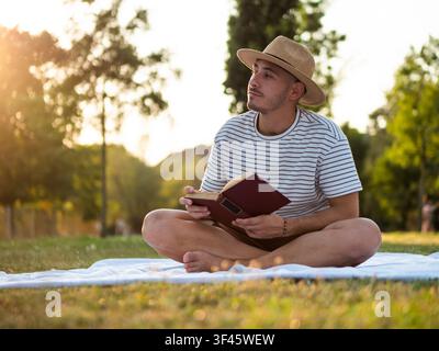 Young man enjoys sunset while reading a book in a park. Stock Photo