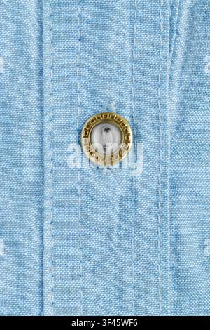 Small golden clothes button on light blue cotton fabric as a background Stock Photo