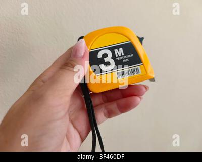 Woman holding a yellow three meter professional tape measure tool in hand Stock Photo