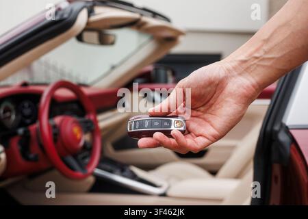 Ljubljana, Slovenia - 2 June 2026: A hand is holding a Porsche 911 Targa 4S car key with the sports car parked behind it. Stock Photo