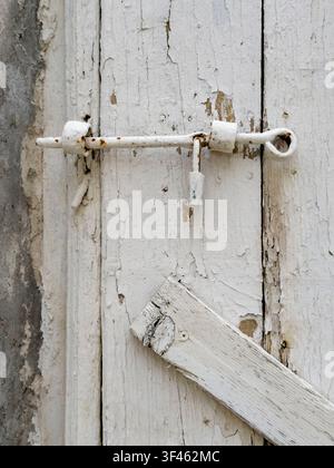 Weathered Door, close up of a wooden door with a metal bolt and padlock, peeling white paint. Stock Photo