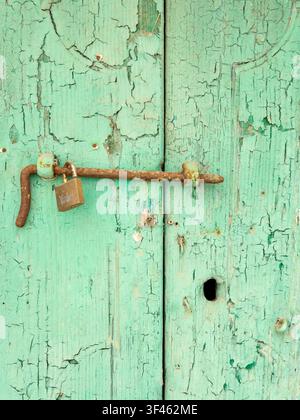Weathered Door with a metal bolt and padlock, green peeling paint, in the town of Pisticci Stock Photo
