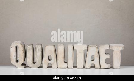 Quality Meaning From German Word QUALITAET Shown With Minimal Concrete Typography On Background Stock Photo