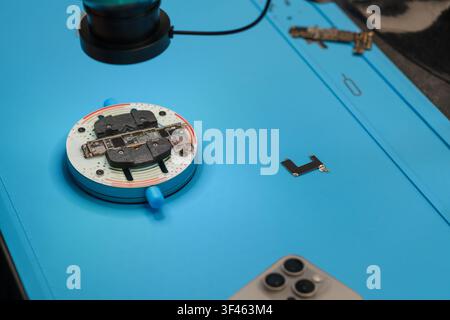 Microscope examining electronic circuit board on blue work surface with smartphone placed nearby, showcasing detailed components and tools Stock Photo