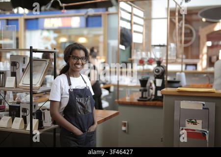 Friendly young barista smiling in her modern coffee shop Stock Photo