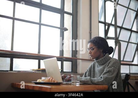 Focused woman working on laptop by a window Stock Photo