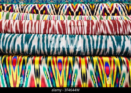 Colorful ikat fabric rolls stacked at a traditional bazaar in Bukhara, Uzbekistan. Vibrant silk textiles with classic Central Asian patterns ideal for Stock Photo