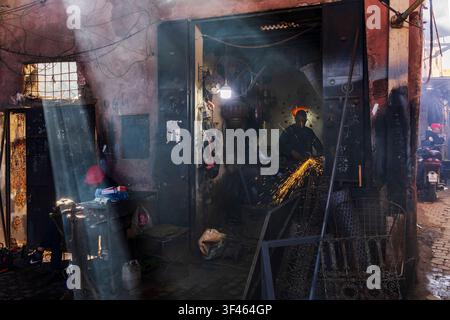 A small metalwork workshop in a souk, a man using a grinder creating sparks, light filtering through small window. Stock Photo