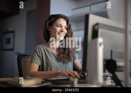Happy young woman smiling while working on a computer at home Stock Photo