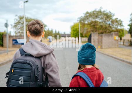 Boy and girl walking toward a school with backpacks Stock Photo