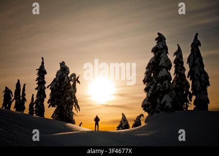 Person silhouetted on snowy mountain at sunset Stock Photo