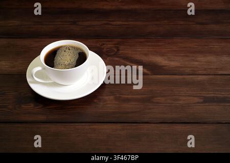 Porcelain Coffee Cup with Frothy Black Coffee on Rustic Wooden Table Stock Photo