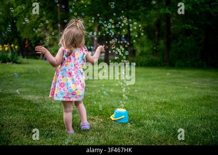 Toddler girl plays with bubbles in a backyard Stock Photo