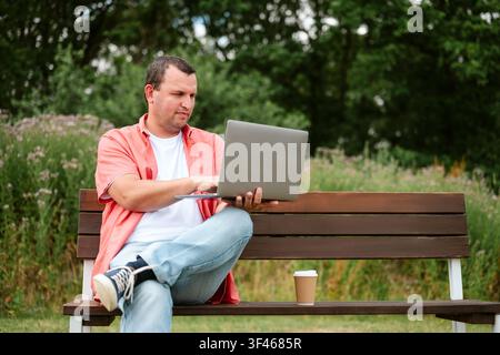 Man working on laptop while sitting on park bench, copy space Stock Photo